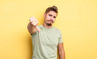 Huysuz, sinirli, sinirli, hayal kırıklığına uğramış ya da hoşnutsuz genç bir adam ciddi bir bakışla baş parmağını aşağı gösteriyor. Garip bıyık konsepti