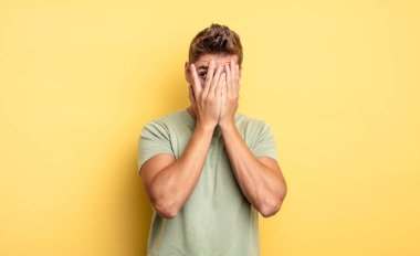 Genç yakışıklı adam elleriyle yüzünü kapatıyor, parmaklarının arasından şaşkın bir ifadeyle yan tarafa bakıyor. Garip bıyık konsepti