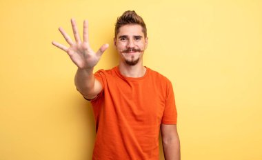 Genç, yakışıklı bir adam gülümsüyor ve arkadaş canlısı görünüyor. Beş ya da beş numarayı gösteriyor. Eli önde, geri sayıyor. Garip bıyık konsepti