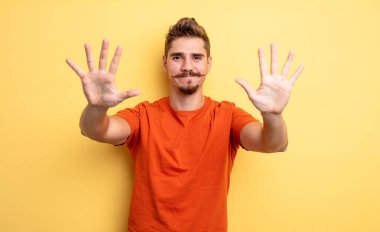 Genç yakışıklı adam gülümsüyor ve arkadaş canlısı görünüyor, onuncu ya da onuncu numarayı gösteriyor, eli önde, geriye doğru sayıyor. Garip bıyık konsepti