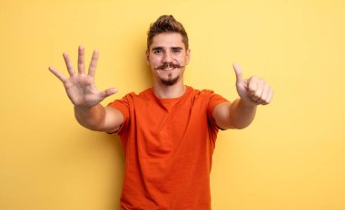 Genç yakışıklı adam gülümsüyor ve arkadaş canlısı görünüyor. Altı ya da altıncı numarayı gösteriyor. Elleri önde, geriye doğru sayıyor. Garip bıyık konsepti