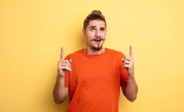 Genç yakışıklı adam şaşırmış, şaşırmış ve ağzı açık görünüyor, iki eliyle uzayı kopyalamak için yukarı bakıyor. Garip bıyık konsepti