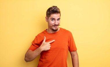 Genç yakışıklı adam mutlu, gururlu ve şaşırmış görünüyor, neşeli bir şekilde kendini gösteriyor, kendinden emin ve kibirli hissediyor. Garip bıyık konsepti