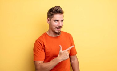 Genç ve yakışıklı bir adam heyecanlı ve şaşırmış görünüyor. Yana ve yukarı doğru uzayı işaret ediyor. Garip bıyık konsepti