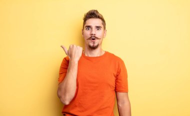 Genç ve yakışıklı bir adam inançsızlıktan şaşkın şaşkın bakıyor, yan taraftaki objeyi işaret ediyor ve 