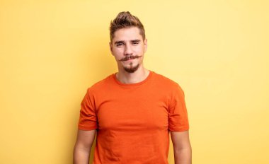 Genç yakışıklı adam, olumlu ve kendinden emin bir şekilde gülümsüyor. Tatmin olmuş, arkadaş canlısı ve mutlu görünüyor. Garip bıyık konsepti