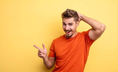 Genç yakışıklı adam gülüyor, mutlu, pozitif ve şaşırmış görünüyor, yanal fotokopi alanını işaret eden harika bir fikrin farkına varıyor. Garip bıyık konsepti