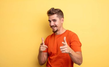 Olumlu, başarılı ve mutlu bir tavırla gülümseyen genç yakışıklı adam kamerayı işaret ediyor, elleriyle silah işareti yapıyor. Garip bıyık konsepti