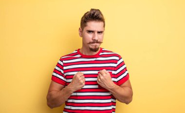 Kendinden emin, sinirli, güçlü ve agresif, boks pozisyonunda dövüşmeye hazır genç yakışıklı bir adam. Garip bıyık konsepti