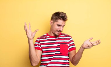 young handsome man shrugging with a dumb, crazy, confused, puzzled expression, feeling annoyed and clueless. strange moustache concept