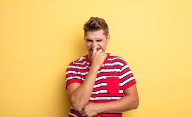 Genç yakışıklı adam iğreniyor, kötü ve nahoş bir kokuyu koklamamak için burnunu tutuyor. Garip bıyık konsepti