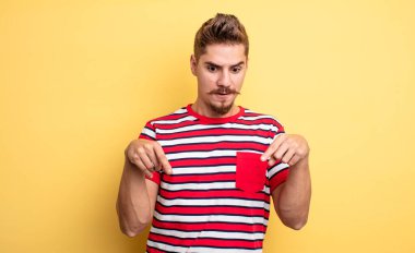 Genç yakışıklı adam şok olmuş, ağzı açık ve şaşkın, inançsızlık ve şaşkınlık içinde bakıyor ve aşağı doğru işaret ediyor. Garip bıyık konsepti