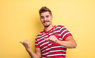 Genç yakışıklı adam neşeyle gülümsüyor ve yan taraftaki fotokopi alanını gösteriyor, mutlu ve tatmin olmuş hissediyor. Garip bıyık konsepti