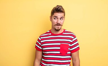 Genç yakışıklı adam şok olmuş, mutlu, şaşkın ve şaşırmış hissediyor, ağzı açık bir şekilde yana bakıyor. Garip bıyık konsepti