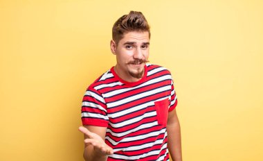 Genç, yakışıklı bir adam gülümsüyor, mutlu görünüyor, kendinden emin ve arkadaş canlısı, bir anlaşmaya varmak için el sıkışmayı teklif ediyor, işbirliği yapıyor. Garip bıyık konsepti