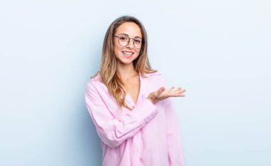 pretty caucasian woman smiling cheerfully, feeling happy and showing a concept in copy space with palm of hand