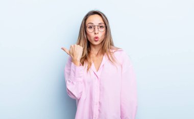 pretty caucasian woman looking astonished in disbelief, pointing at object on the side and saying wow, unbelievable