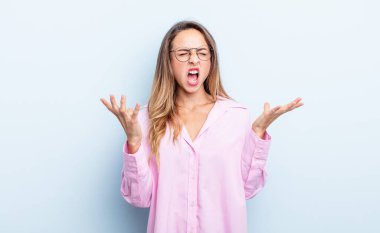 pretty caucasian woman furiously screaming, feeling stressed and annoyed with hands up in the air saying why me