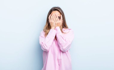 pretty caucasian woman feeling scared or embarrassed, peeking or spying with eyes half-covered with hands