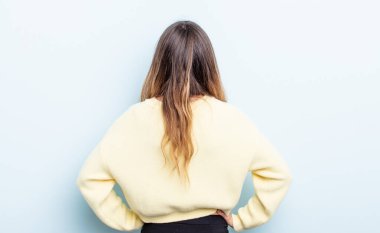pretty caucasian woman feeling confused or full or doubts and questions, wondering, with hands on hips, rear view