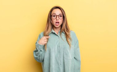 pretty caucasian woman looking shocked and surprised with mouth wide open, pointing to self