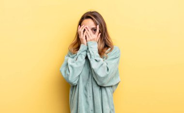 pretty caucasian woman feeling scared or embarrassed, peeking or spying with eyes half-covered with hands