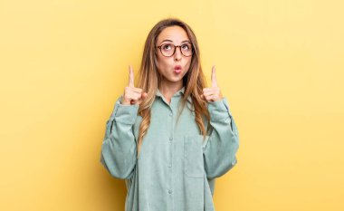 pretty caucasian woman feeling awed and open mouthed pointing upwards with a shocked and surprised look