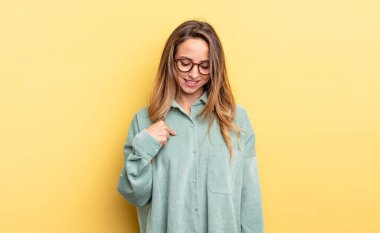 pretty caucasian woman smiling cheerfully and casually, looking downwards and pointing to chest