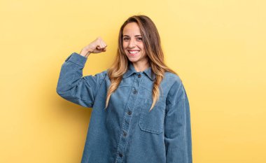 pretty caucasian woman feeling happy, satisfied and powerful, flexing fit and muscular biceps, looking strong after the gym