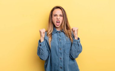 pretty caucasian woman shouting aggressively with an angry expression or with fists clenched celebrating success
