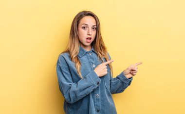 pretty caucasian woman feeling shocked and surprised, pointing to copy space on the side with amazed, open-mouthed look