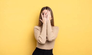 pretty caucasian woman covering face with hands, peeking between fingers with surprised expression and looking to the side