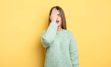 pretty caucasian woman looking sleepy, bored and yawning, with a headache and one hand covering half the face