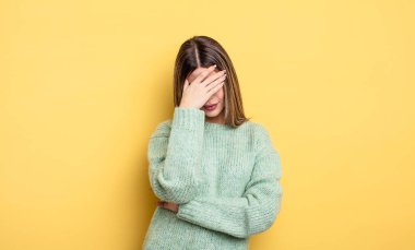 pretty caucasian woman looking stressed, ashamed or upset, with a headache, covering face with hand