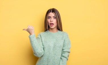 pretty caucasian woman looking astonished in disbelief, pointing at object on the side and saying wow, unbelievable