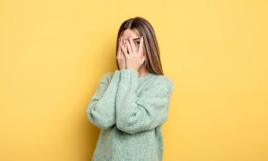 pretty caucasian woman feeling scared or embarrassed, peeking or spying with eyes half-covered with hands