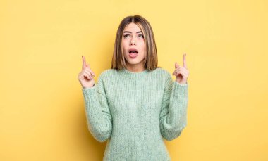 pretty caucasian woman feeling awed and open mouthed pointing upwards with a shocked and surprised look