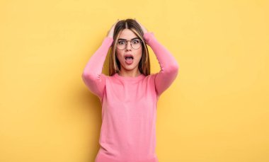 pretty caucasian woman looking unpleasantly shocked, scared or worried, mouth wide open and covering both ears with hands