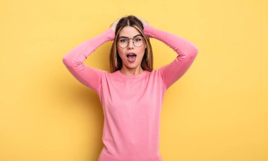 pretty caucasian woman raising hands to head, open-mouthed, feeling extremely lucky, surprised, excited and happy