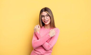 pretty caucasian woman smiling cheerfully and celebrating, with fists clenched and arms crossed, feeling happy and positive