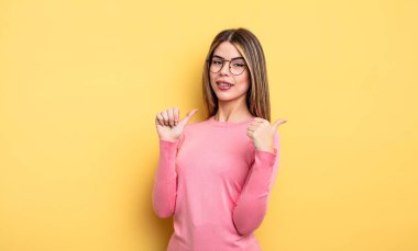 pretty caucasian woman smiling cheerfully and casually pointing to copy space on the side, feeling happy and satisfied