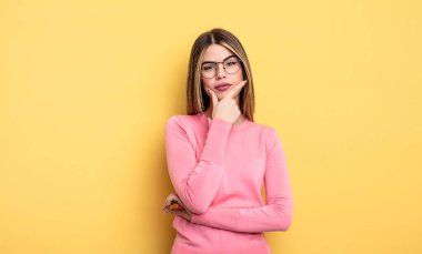 Kafkasyalı bir kadın ciddi, düşünceli ve güvensiz görünüyor, bir kolu çapraz ve çenesi üzerinde, seçenekleri tartıyor.