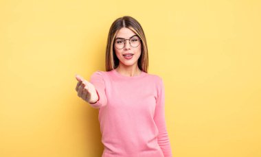 Güzel, beyaz bir kadın gülümsüyor, mutlu görünüyor, kendinden emin ve arkadaş canlısı, anlaşmaya varmak için el sıkışmayı teklif ediyor, işbirliği yapıyor.