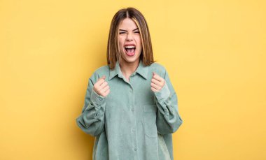 pretty caucasian woman shouting aggressively with annoyed, frustrated, angry look and tight fists, feeling furious