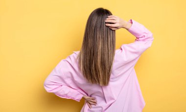 pretty caucasian woman thinking or doubting, scratching head, feeling puzzled and confused, back or rear view