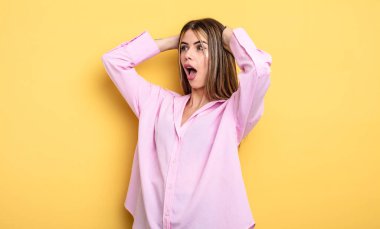 pretty caucasian woman with open mouth, looking horrified and shocked because of a terrible mistake, raising hands to head
