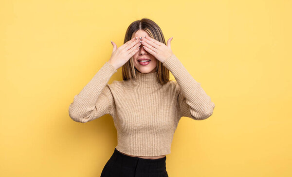 pretty caucasian woman smiling and feeling happy, covering eyes with both hands and waiting for unbelievable surprise