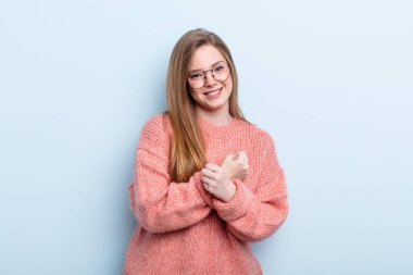 Kafkasyalı kızıl saçlı kadın, neşeli bir şekilde gülümsüyor ve kutluyor, yumruklarını sıkıp kollarını kavuşturuyor, mutlu ve pozitif hissediyor.