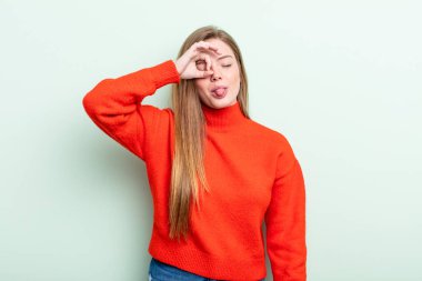 Kafkasyalı kızıl saçlı kadın komik yüzüyle mutlu bir şekilde gülümsüyor, şaka yapıyor ve gözetleme deliğinden bakıyor, sırları gözetliyor.