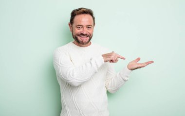 Orta yaşlı yakışıklı adam gülümsüyor, mutlu, kaygısız ve tatmin olmuş hissediyor, fotokopi alanındaki konsepte ya da fikre işaret ediyor.